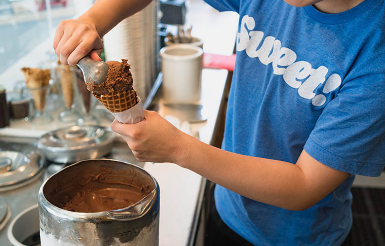 scooping chocolate ice cream into a waffle cone