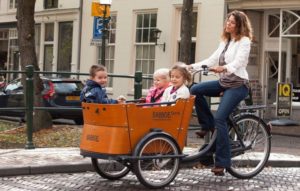 woman riding babboe curve bicycle with 3 children in the front carriage